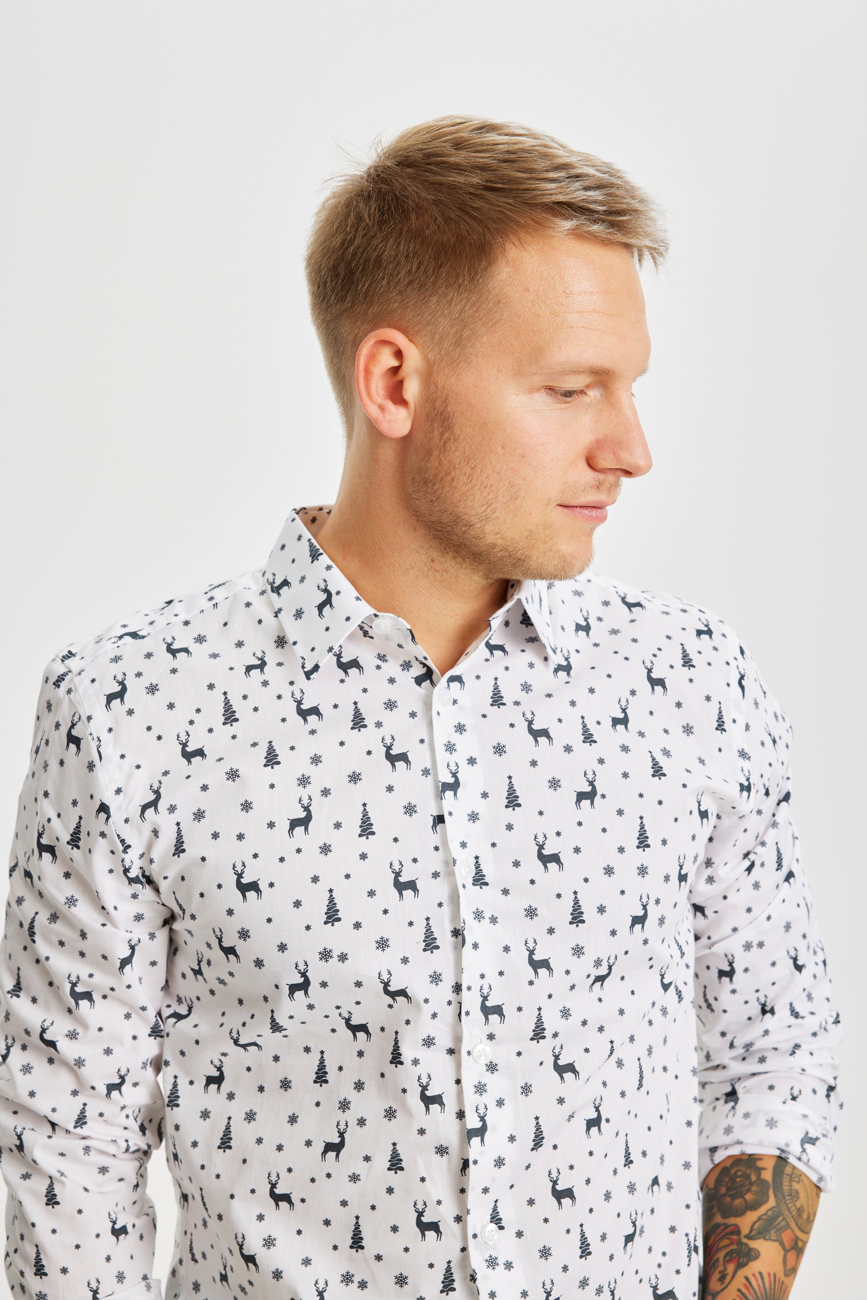 Ein Mann, der zur Seite schaut und ein weißes Weihnachtshemd mit Weihnachtsmuster trägt.